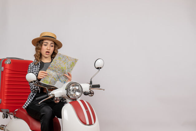 骑坐在轻便摩托车上困惑的年轻女子看着灰色的地图地图车辆摩托车