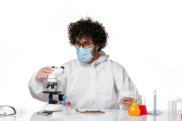 视图男医生穿着防护服 戴着口罩 用显微镜观察浅白色光套装医生