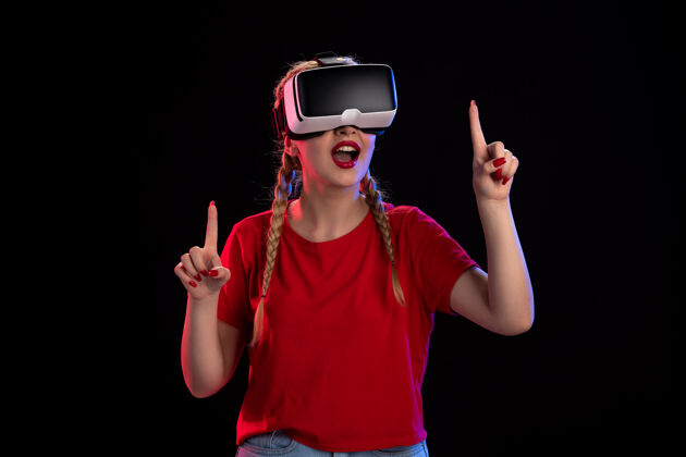 人物年轻女性在黑暗的墙上玩虚拟现实的正面图游戏虚拟现实年轻女性