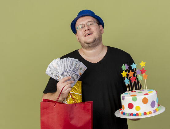 穿快乐的成年斯拉夫人戴着眼镜 戴着蓝色派对帽 手里拿着钱礼盒 纸购物袋和生日蛋糕钱复制橄榄