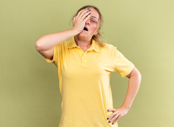女人穿着黄色衬衫的不健康妇女站在绿色墙壁上 感觉不舒服 摸了摸额头 头晕 感冒头晕站立不适