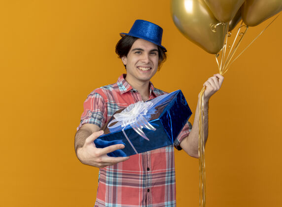 男人面带微笑的白人帅哥头戴蓝色派对帽手持氦气球和礼盒盒子礼物聚会