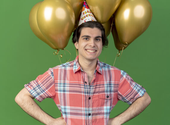 前面笑容可掬的高加索帅哥戴着生日帽站在氦气球前空间穿氦