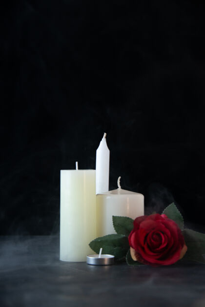 蜡烛在黑暗的墙上 白色的蜡烛和红色的玫瑰作为记忆的正视图红色葬礼玫瑰