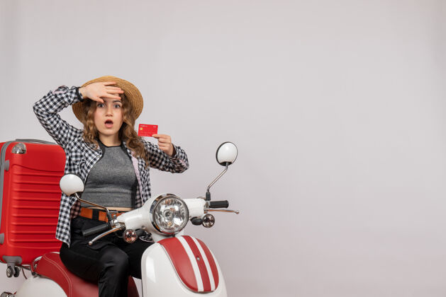 困惑的年轻女子困惑的年轻女子骑着轻便摩托车 手里拿着灰色的卡片车辆摩托车摩托车