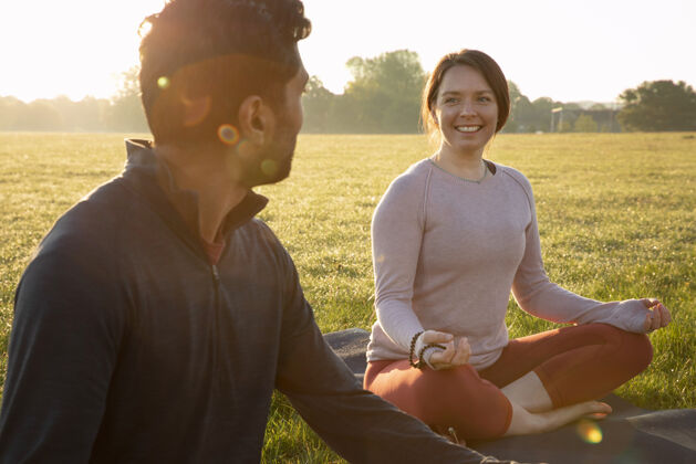 女人微笑的女人和男人在户外瑜伽垫上冥想男人瑜伽垫外面
