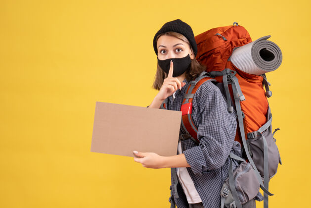 背包带着黑色面具和背包的旅行女孩拿着纸板做了一个安静的标志黑人男人人