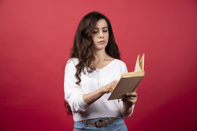 休闲年轻女子在红色背景上读一本有趣的书高质量的照片肖像手持女性