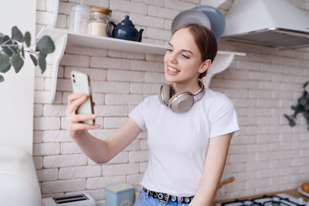 特写穿着休闲装的年轻美女戴着耳机坐在厨房的桌子上打视频电话微笑肖像厨房
