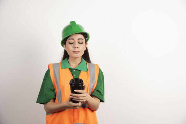 人年轻的女建造师在看黑色的杯子高品质的照片咖啡头盔安全帽