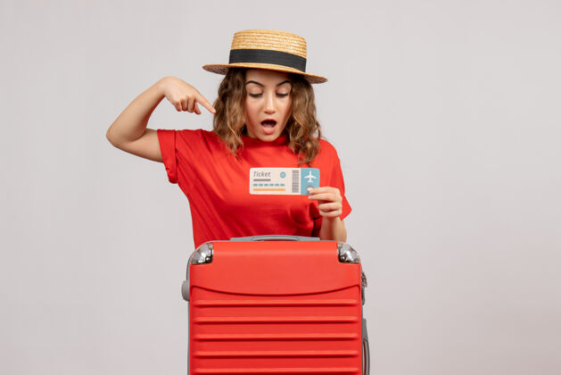 帽子带着旅行箱指着车票的度假女孩感到惊奇休闲女人指点
