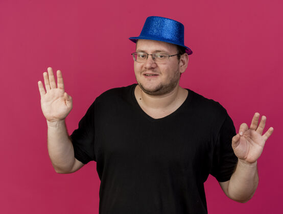 好的高兴的成年斯拉夫男子戴着眼镜戴着蓝色派对帽用双手做手势表示同意眼镜派对手