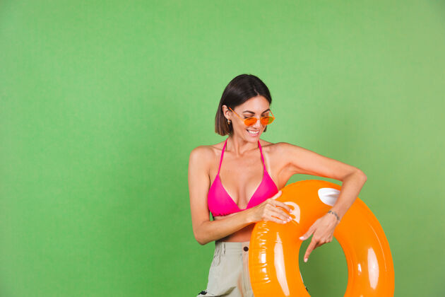 娱乐夏日修身运动型女士 粉色比基尼 亮橙色充气戒指 圆形墨镜 绿色 快乐积极肖像浮子放松