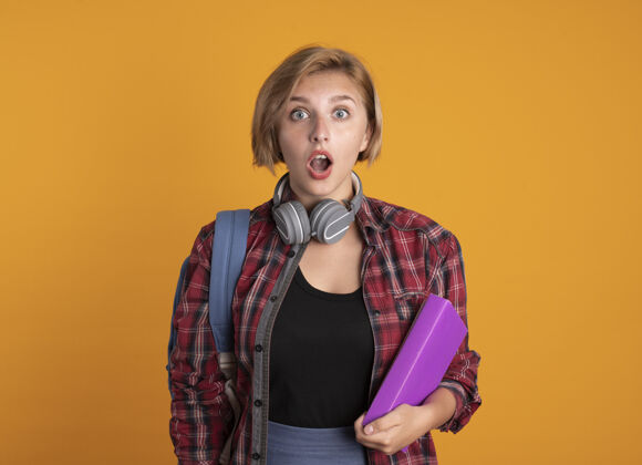 复制震惊的年轻斯拉夫女学生戴着耳机背着书包拿着书和笔记本笔记本空间背包