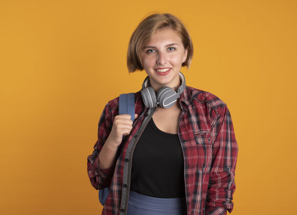 年轻微笑的年轻斯拉夫女学生戴着耳机背着背包看着镜头穿学生背包