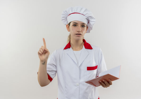 印象年轻漂亮的厨师穿着厨师制服 拿着便笺簿 举起手指孤立地站在白色的墙上拿着漂亮手指