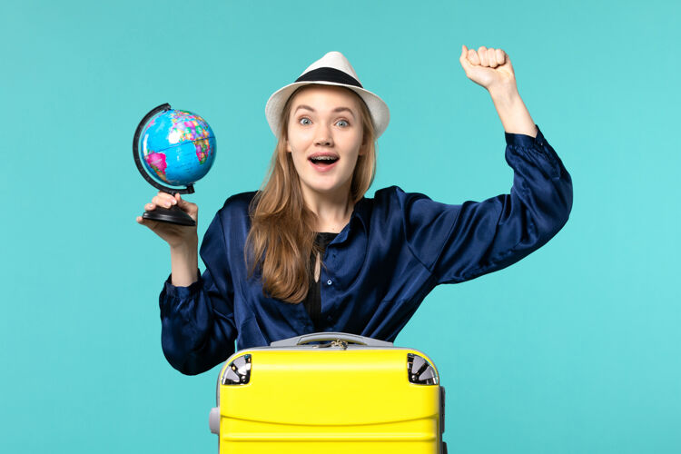 人前视图年轻女子拿着地球仪 准备在蓝色背景上度假女性旅行航海飞机度假女地球球