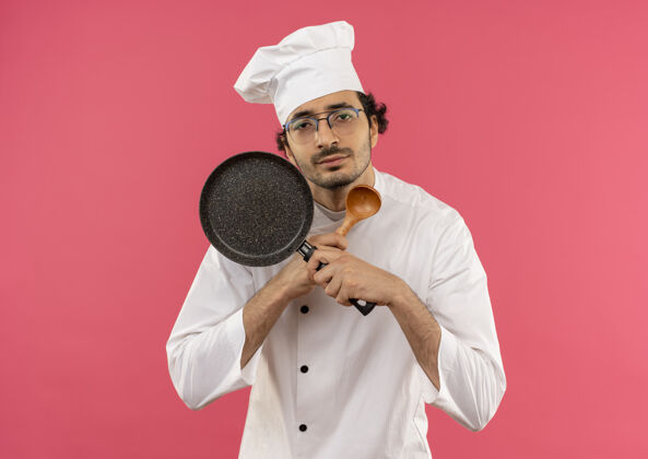 薯条看起来年轻的男厨师穿着厨师制服 戴着眼镜 拿着勺子 拿着煎锅穿制服平底锅