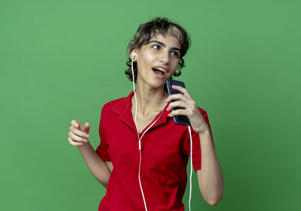 绿色唱歌的年轻白种女孩 披着小精灵的发型 戴着耳机 用手机当麦克风看着身边使用穿复制