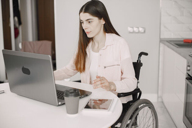 商务女性一位年轻漂亮的残疾妇女坐在轮椅上 在家里用笔记本电脑工作 远程工作办公室水平商务人士