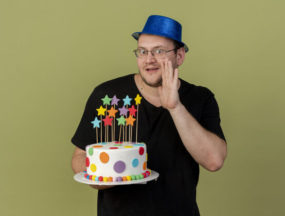 蛋糕一个戴着眼镜 戴着蓝色派对帽的成年斯拉夫人惊讶地把手放在嘴边 拿着生日蛋糕看着镜头蓝色保留空格
