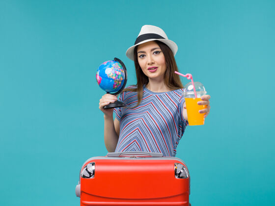 地球仪前景度假中的女人拿着果汁和地球仪在蓝色的背景海上航行度假暑假旅行旅行旅程航行