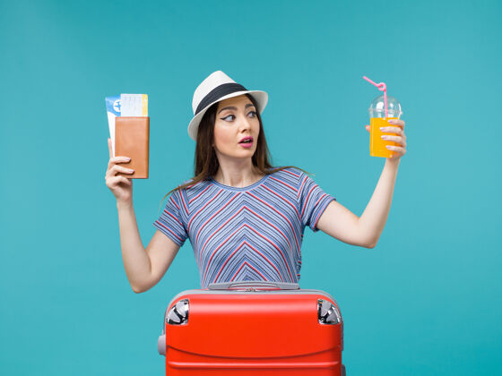 举行前景度假中的女人拿着她的果汁和浅蓝色背景的机票去度假帽子肖像航行