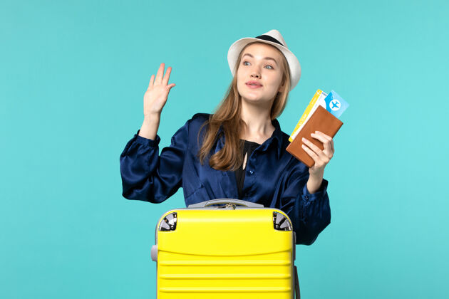 年轻女子前视图年轻女子拿着机票 准备乘坐浅蓝色背景的旅行海上度假旅行飞机远航人航行美丽