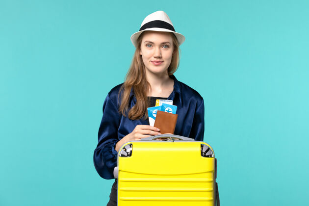 微笑正面图年轻女子拿着她的机票 准备乘坐蓝色背景的旅行飞机出海度假旅行人美丽旅行