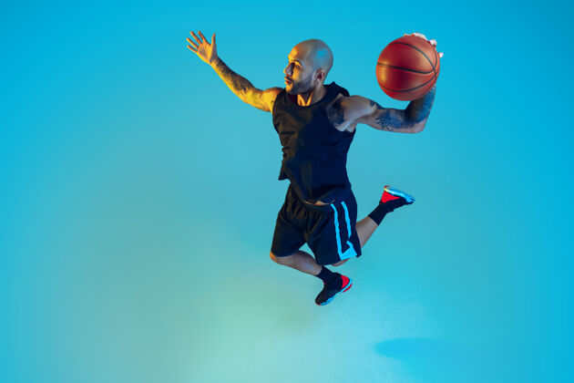 运动员年轻的篮球队员穿着运动服训练 在运动中练习 在霓虹灯下的蓝色墙壁上运动大满贯肌肉活跃