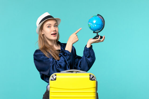 手持前视图年轻女子手持地球仪 准备在淡蓝色背景飞机上度假女性度假之旅远航大海旅程地球仪女性