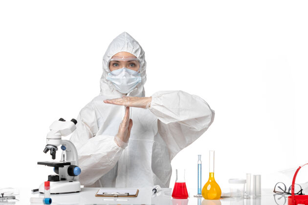 专业正面图年轻女医生穿着白色防护服 戴着口罩 因为covid显示白色背景上的t字母病毒大流行飞溅covid-信件医生药品