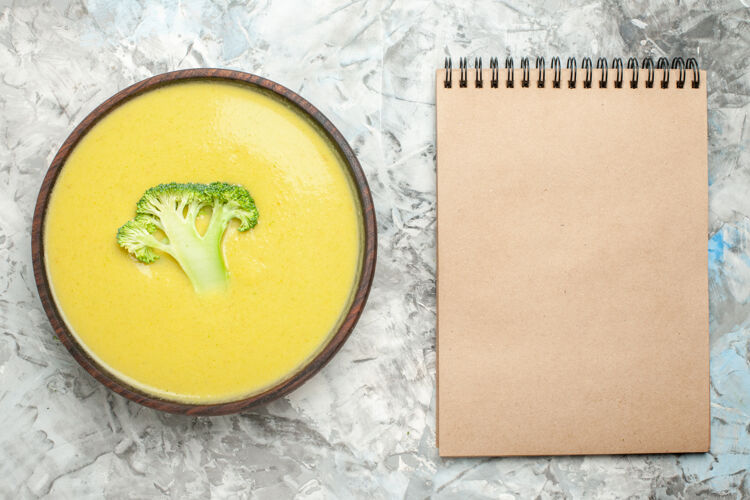 食物奶油西兰花汤在棕色碗和白色背景上的笔记本俯视图膳食晚餐营养