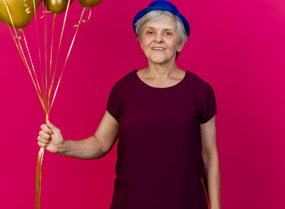 粉色微笑的老妇人戴着聚会帽 手里拿着粉红色的氦气球帽子女人穿