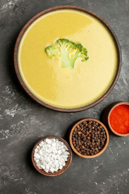 香料棕色碗里的奶油西兰花汤和灰色桌子上的不同香料的垂直视图健康不同午餐