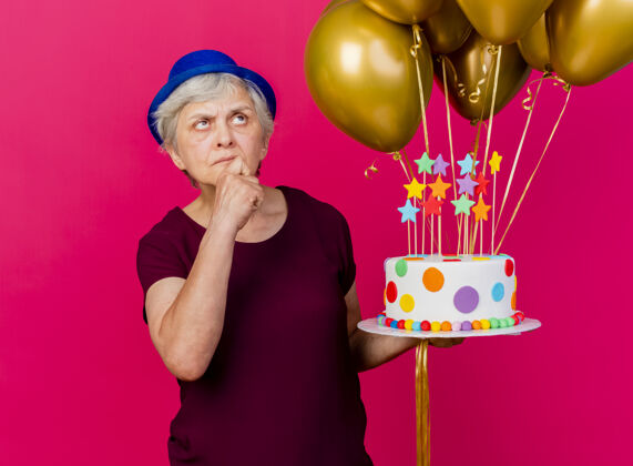 向上困惑的老妇人戴着聚会帽 手里拿着氦气球和生日蛋糕老人气球手