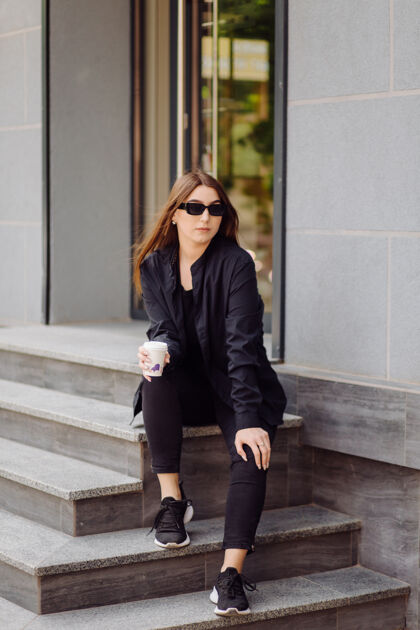 购物户外生活写真迷人的黑发女孩喝咖啡 走在城市街道上衣服夹克杯子