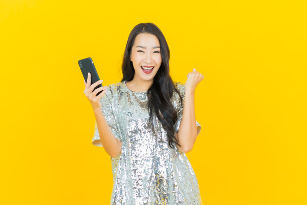 聪明肖像美丽的亚洲年轻女子微笑着智能手机上的黄色设备手指电话