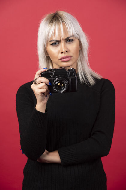 人类美丽的年轻女子手持相机站在红色背景下高品质的照片女性摄影师年轻人