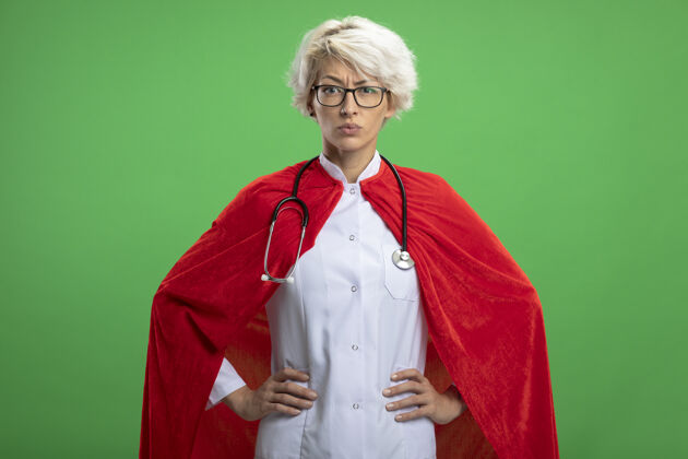 光学穿着医生制服的严肃的斯拉夫超级英雄女人 戴着红斗篷和戴着眼镜的听诊器超级英雄女人听诊器
