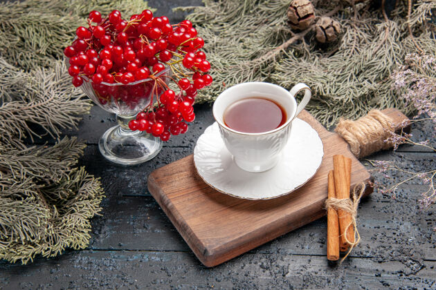 冷杉底图：一杯红醋栗 一杯茶 一块肉桂 在砧板上 在黑暗的背景下 还有冷杉树枝茶背景板