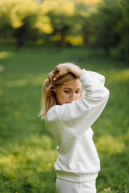 时髦年轻的金发女孩穿着白色连帽衫 微笑着走在树林里广告纺织品衣服