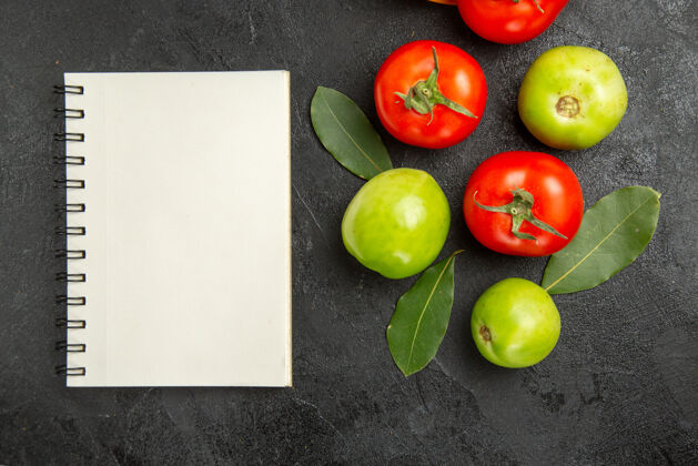 食物顶视图红色和绿色的西红柿月桂叶和一个笔记本在黑暗的表面苹果香草成熟