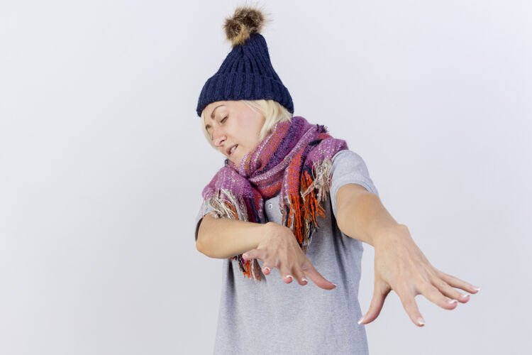 帽子恼怒的年轻金发病女人戴着冬天的帽子和围巾伸出双手孤立在白墙上人姿势疾病