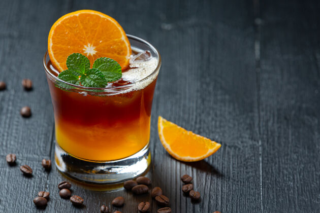 温暖橘子和咖啡鸡尾酒在黑暗的表面上分层热带液体