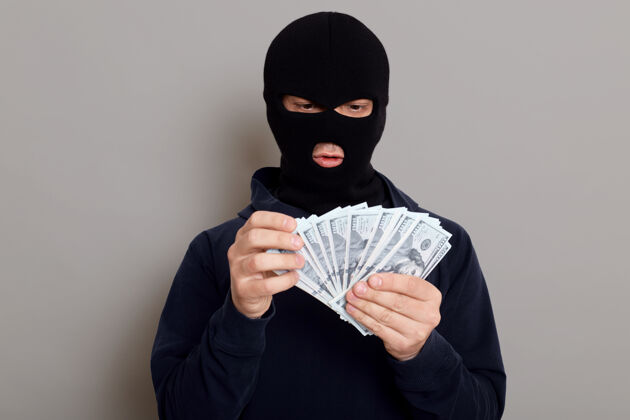非法一个穿着黑色连帽衫的劫匪站在那里 伪装成一张脸 手里拿着很多钱金钱恶棍不法分子