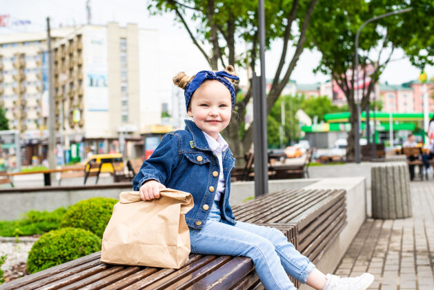孩子年轻的小女孩拿着快餐袋坐在咖啡馆旁边的长凳上可爱女孩可爱
