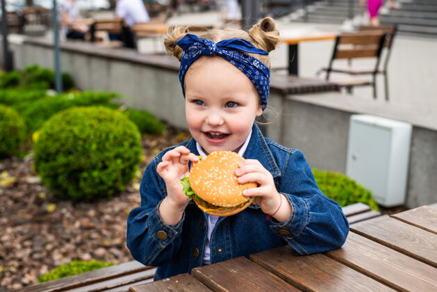 可爱在一个阳光明媚的日子里 一个迷人的微笑着的小女孩在户外拿着一个汉堡包孩子餐厅小女孩