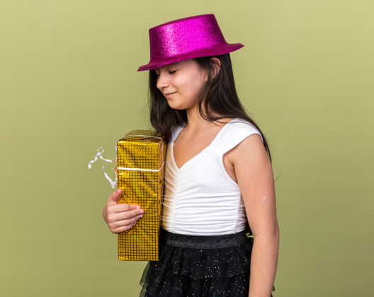 生日令人高兴的年轻白人女孩 戴着紫色派对帽 手拿礼品盒 孤立地放在橄榄绿的墙上 留有复制空间年轻白种人孤立