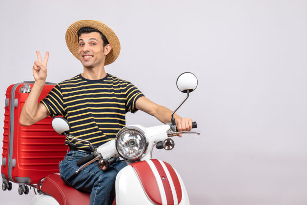 人幸福的年轻人在轻便摩托车上戴着草帽示意胜利标志的正面图摩托车胜利成人